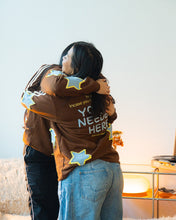 Load image into Gallery viewer, Two people hugging indoors, both wearing brown sweatshirts decorated with blue star patches. The person in front has white text on the back reading 'YOU NEED HELP' and is wearing light blue jeans.

